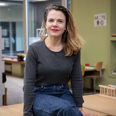 Frau sitzt lächelnd auf einem Tisch in modernem Raum.