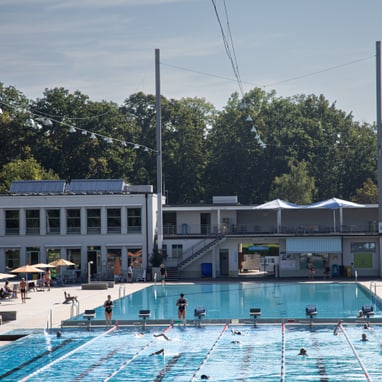 Freibad mit Schwimmern und Gebäuden im Hintergrund.