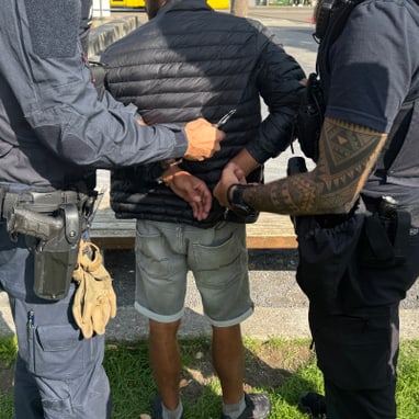 Person wird von zwei Polizisten in Handschellen gelegt.