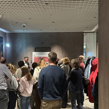 Gruppe von Menschen, die stehend eine Präsentation verfolgen.