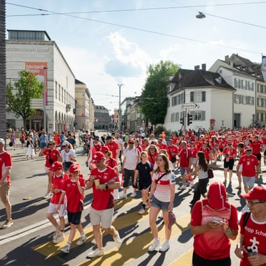 Menschenmenge in roter Kleidung bei einer Strassenparade in der Stadt.