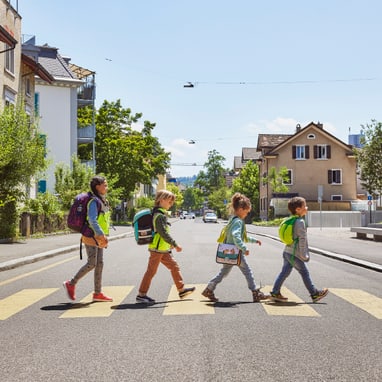 Kinder überqueren Zebrastreifen in Wohnviertel bei Sonne.