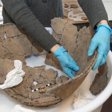 Person in blauen Handschuhen arbeitet an bronzezeitlichen Tonscherben.