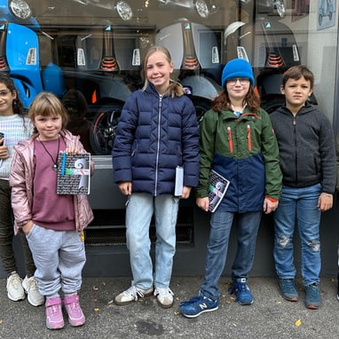 Sechs Kinder stehen vor einem Geschäft mit Rollern im Schaufenster.