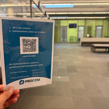 Hand hält einen Flyer in einem modernen Empfangsbereich.
