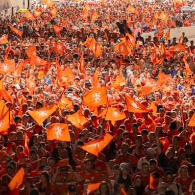 Menschenmenge mit orangefarbenen Fahnen bei einer Veranstaltung im Freien.