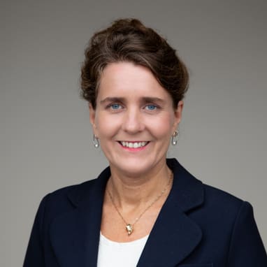 Frau in dunkelblazer vor neutralem Hintergrund.