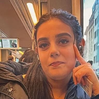 Frau sitzt im Zug und schaut in Richtung Kamera, Fenster im Hintergrund.