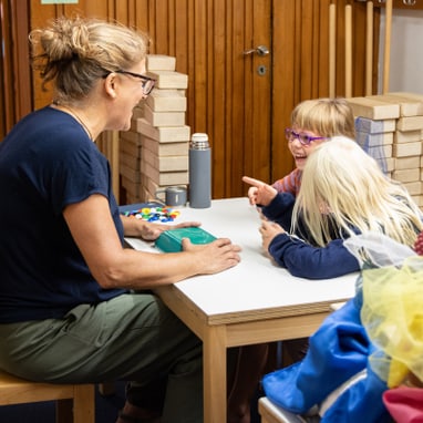 Erwachsener mit zwei Kindern an einem Tisch mit Bauklötzen.
