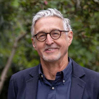 Älterer Mann mit Brille vor grünem Hintergrund.