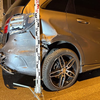 Beschädigtes Auto mit Messlatte und Fahrrad im Hintergrund bei Nacht.