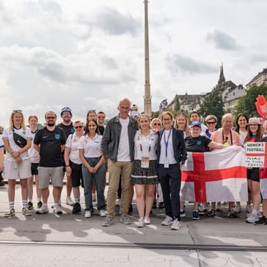 Gruppe von Menschen posiert mit Flagge auf einer Strasse in einer Stadt.