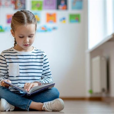 Mädchen liest Buch auf dem Boden sitzend.