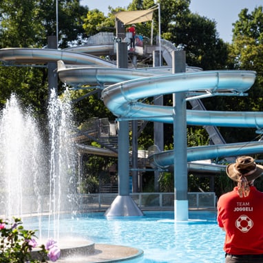 Person im roten Shirt vor Wasserrutsche und Springbrunnen.