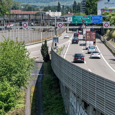 Stadtstrasse neben Bahngleisen mit Verkehr und Graffiti.