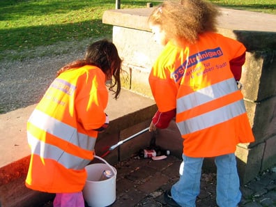 Kinder in neonorangen Westen reinigen einen Park.