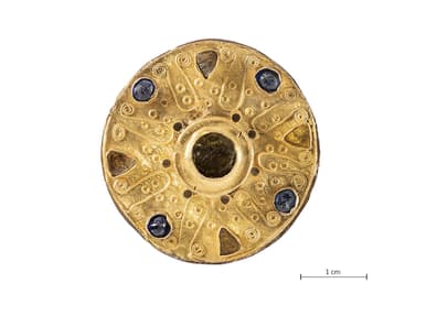 Runde mit grünen Granaten, blauem Glas und Goldauflagen verzierte Scheibenfibel und Massstab 1cm