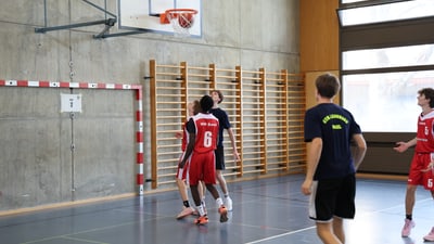 Hallen-Basketballspiel mit Spielern in Aktion am Korb.