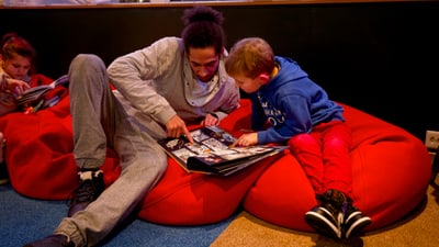 Erwachsener und Kind lesen gemeinsam ein Buch auf roten Sitzsäcken.