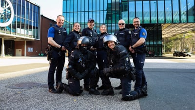 Gruppe von Polizisten posiert vor modernem Gebäude.