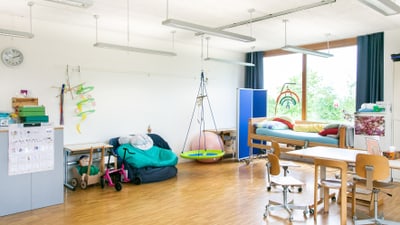 Helles Klassenzimmer mit Spielbereich und Tischgruppe.