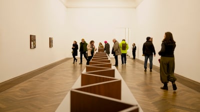 Menschen in einer Kunstgalerie mit Holzinstallation in der Mitte.