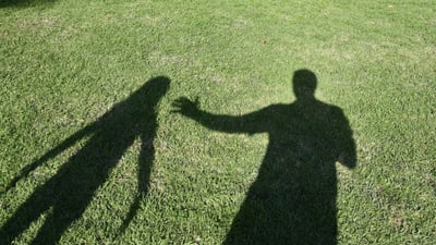 Schatten zweier Personen auf Grasfläche.