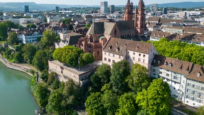 Luftaufnahme des Basler Münsters mit üppig grün bewachsener Pfalz und blauem Rhein.