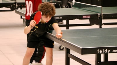 Kind spielt Tischtennis in einer Sporthalle.
