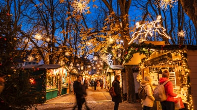 Menschen gehen durch einen geschmückten Weihnachtsmarkt bei Dämmerung.