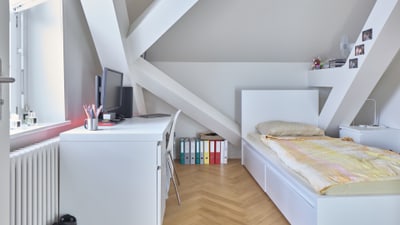 Modernes Schlafzimmer mit Schreibtisch unter geneigter Decke.",