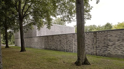 Bäume und eine Mauer, dahinter ein rechteckiges Gebäude.