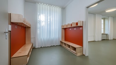 Moderner Umkleideraum mit Holzbänken und roten Wänden.