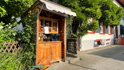 Kleines Holzhäuschen mit Gemüsestand vor einem Wohnhaus.