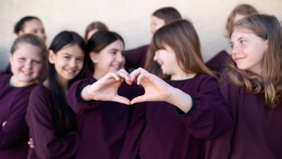 Jugendliche in lila Oberteilen mit Herzhandgeste.