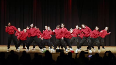 Gruppe von Tänzern in roten Pullovern auf der Bühne.