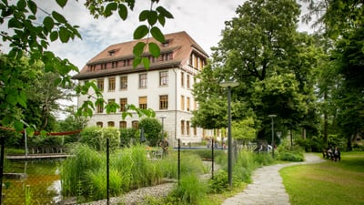 Gebäude hinter Teich und Bäumen im Park.