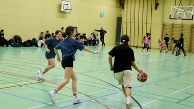 Kinder spielen Basketball in einer Turnhalle.