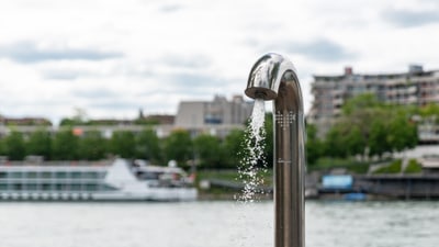 Wasserhahn am Flussufer mit Stadt im Hintergrund.