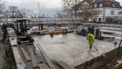 Bauarbeiter reinigt Baustelle mit schwerem Gerät und Materialien im Hintergrund.