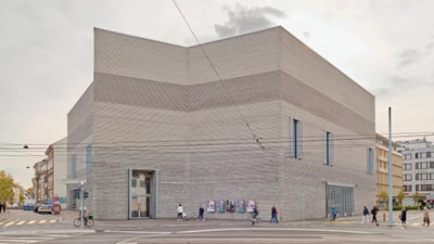 Modernes Gebäude an einer städtischen Strassenkreuzung. Der monumentale Neubau des Kunstmuseums Basel wurde von den Basler Architekten Christ & Gantenbein entworfen. Für Sonderausstellungen und für die Sammlungspräsentation konzipiert, zitiert das Gebäude in vielen seiner Elemente die architektonische Sprache des Hauptbaus von 1936. mit Passanten und Fahrradfahrern.