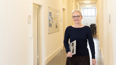 Frau mit Brille, die im Büroflur steht und einen Aktenordner hält.