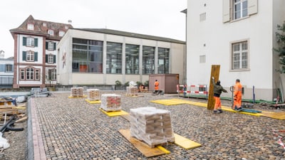 Arbeiter in orangefarbenen Overalls auf einer Pflastersteinstrasse bei Bauarbeiten.