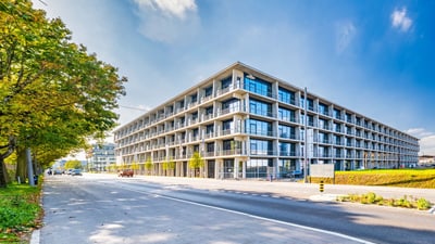 Modernes Gebäude an strassenverkabelter Allee bei sonnigem Wetter.