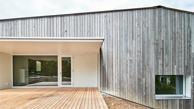 Holzterrasse mit grosser gläserner Verbindungstüre zum Gebäude.