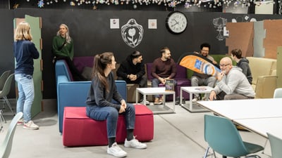 Menschen entspannen in einem modernen Gemeinschaftsraum mit Uhr an der Wand.