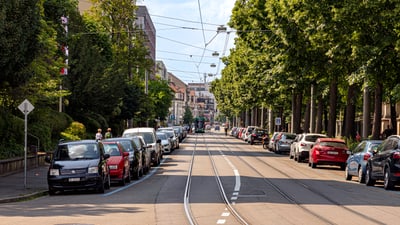 Strasse mit parkenden Autos und Strassenbahngleisen.