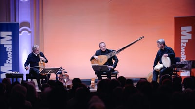 Three musicians on stage with instruments in a concert hall.