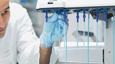 Pharmaceutical employee adjusting laboratory equipment with blue gloves.