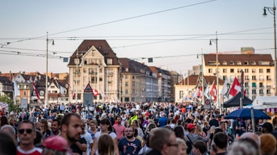 Menschenmenge auf einer belebten Strasse mit historischen Gebäuden.
